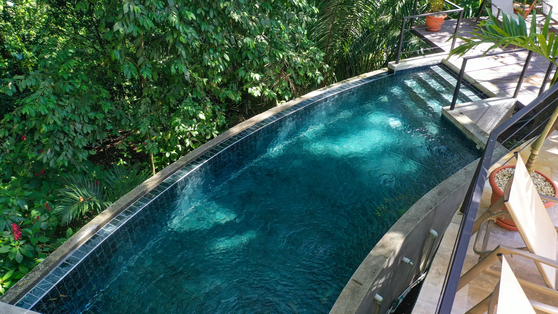 A narrow outdoor pool sits beside a leafy garden and wooden deck.