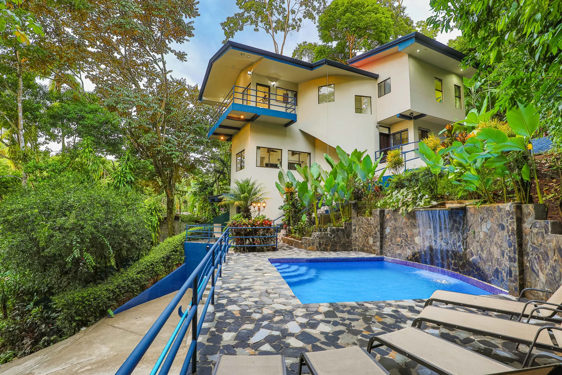 A modern house overlooks a swimming pool, with dense greenery around the terrace.