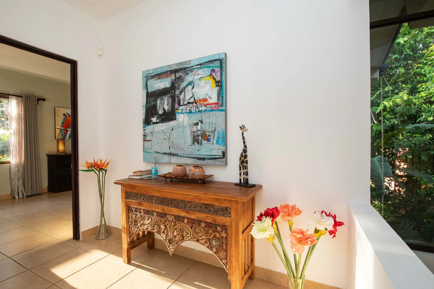 A bright interior with a carved wooden console beneath a colorful painting and flowers.