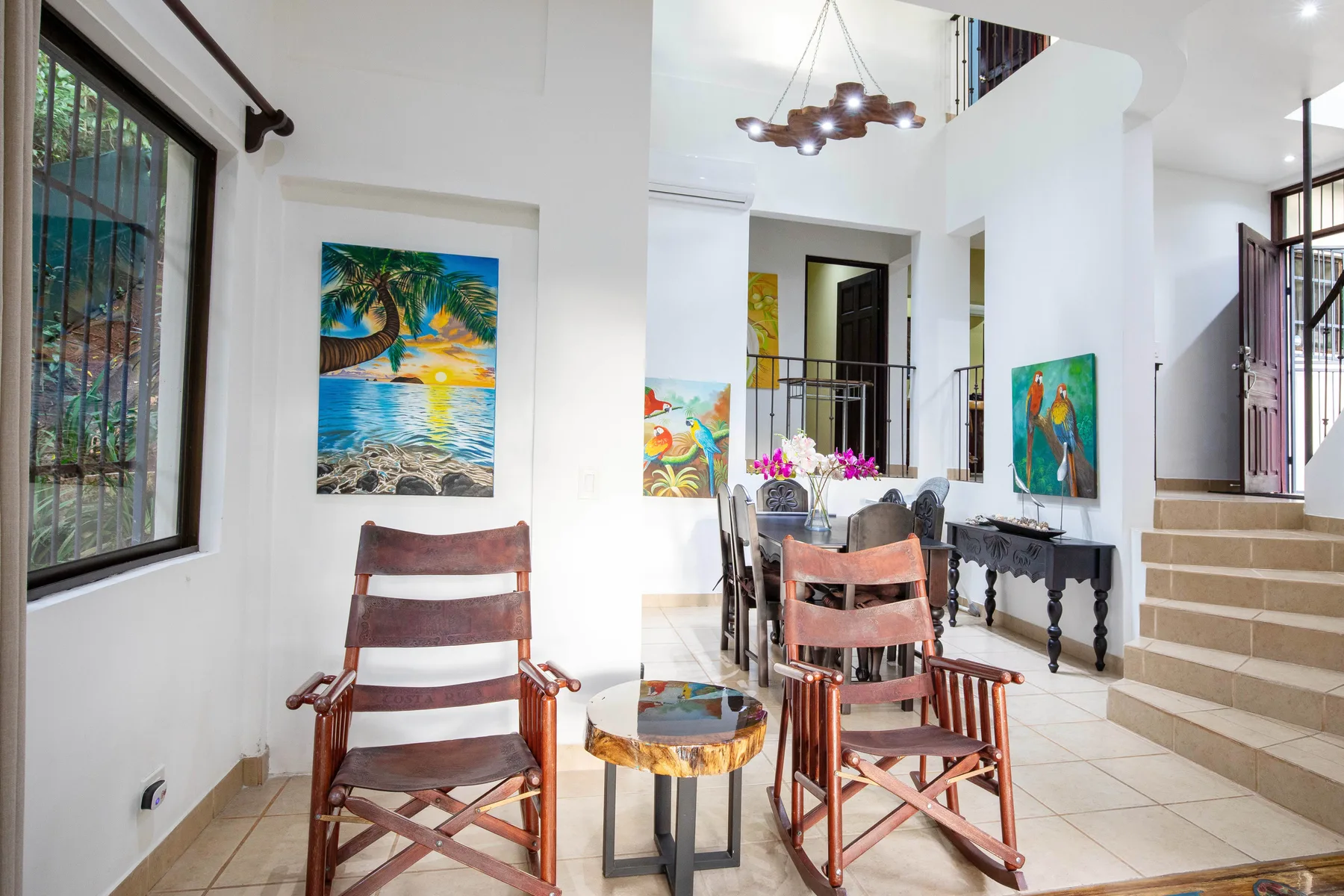 A bright interior seating area with wooden chairs, colorful artwork, and a staircase.