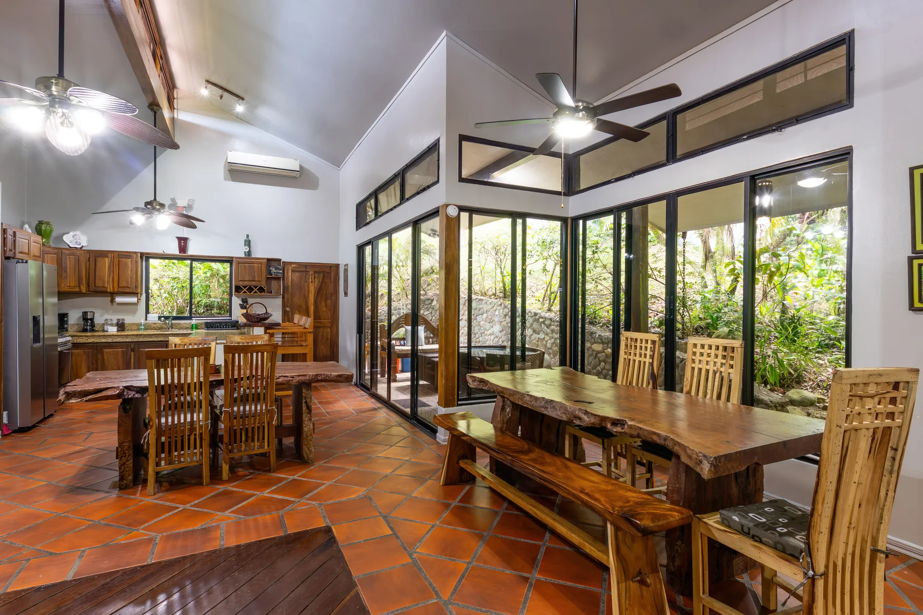 Un comedor abierto con mesas de madera junto a grandes ventanas con vista a la vegetación.