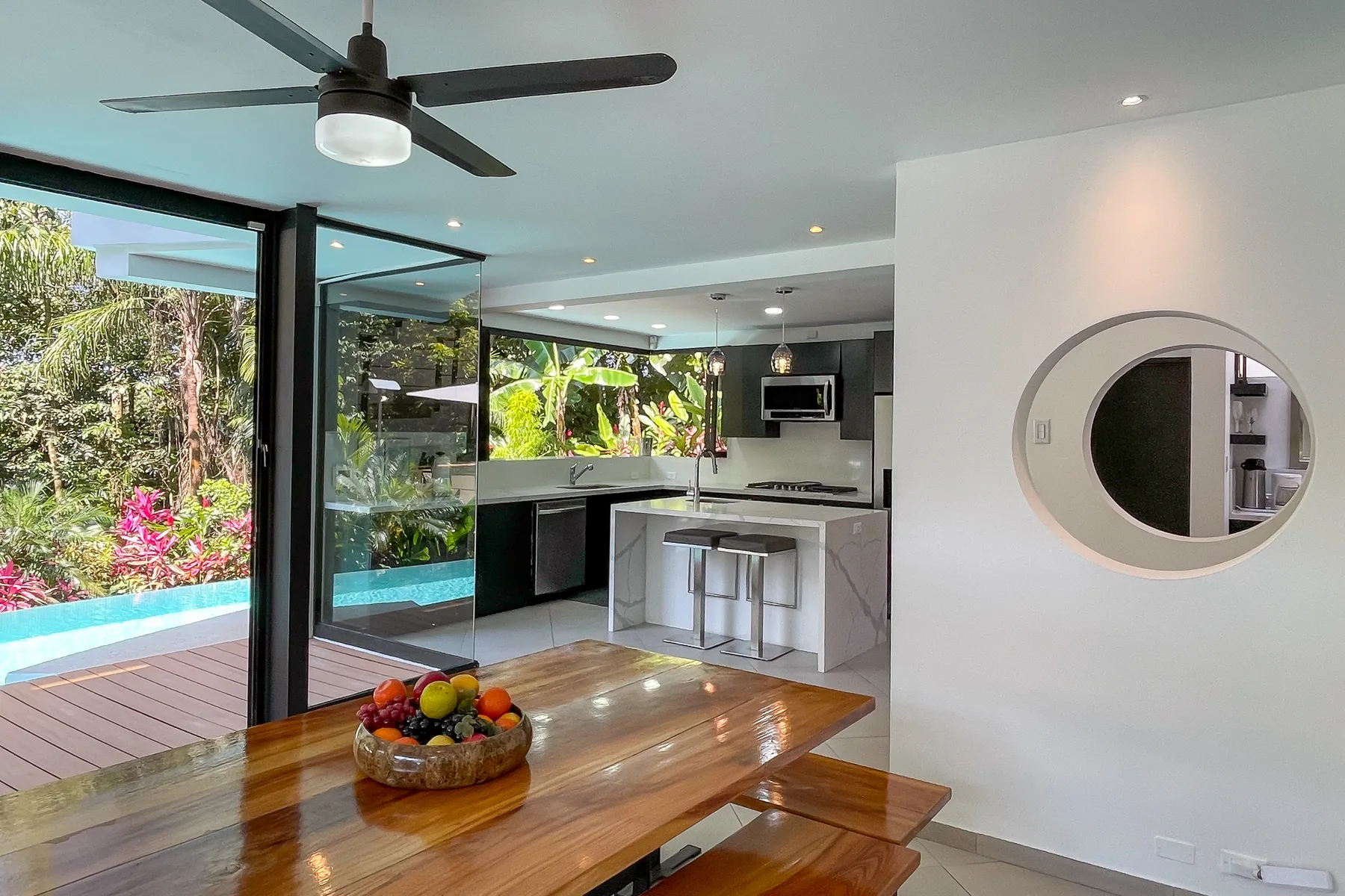 Una cocina y comedor de planta abierta con puertas de vidrio hacia una piscina y un jardín.