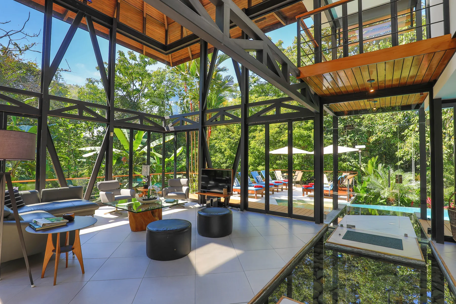 Una luminosa sala con paredes de vidrio se abre a un jardín con piscina.