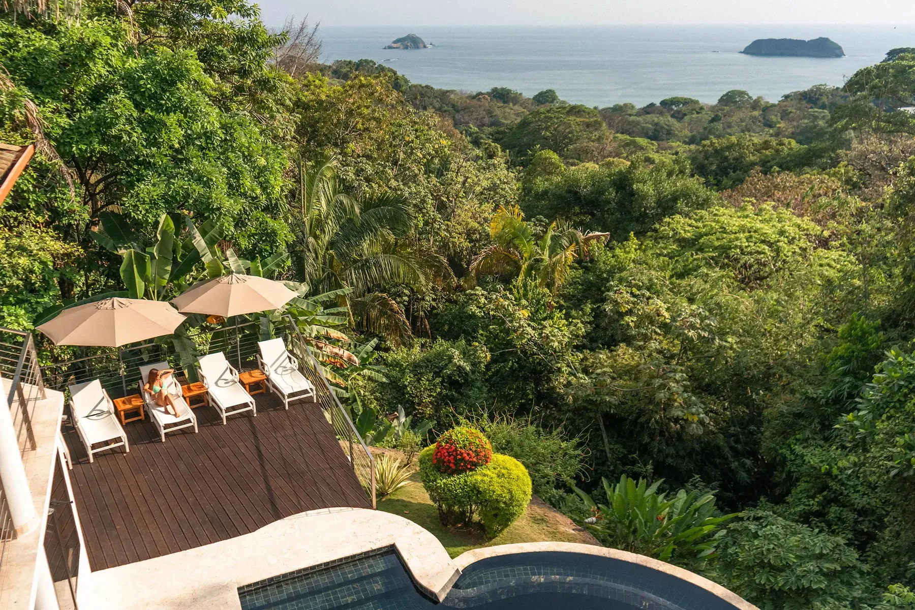 A poolside deck overlooks dense greenery and the ocean.