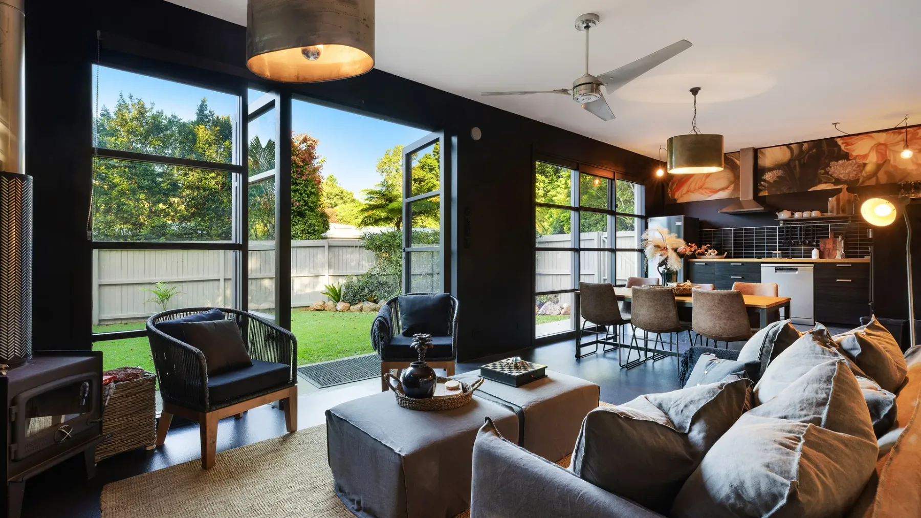 A modern living room opens onto a green garden through large glass doors.