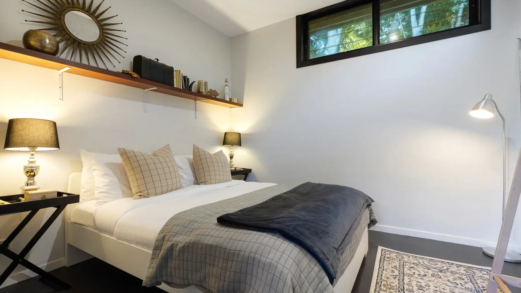 A bedroom with a neatly made bed and a narrow high window.