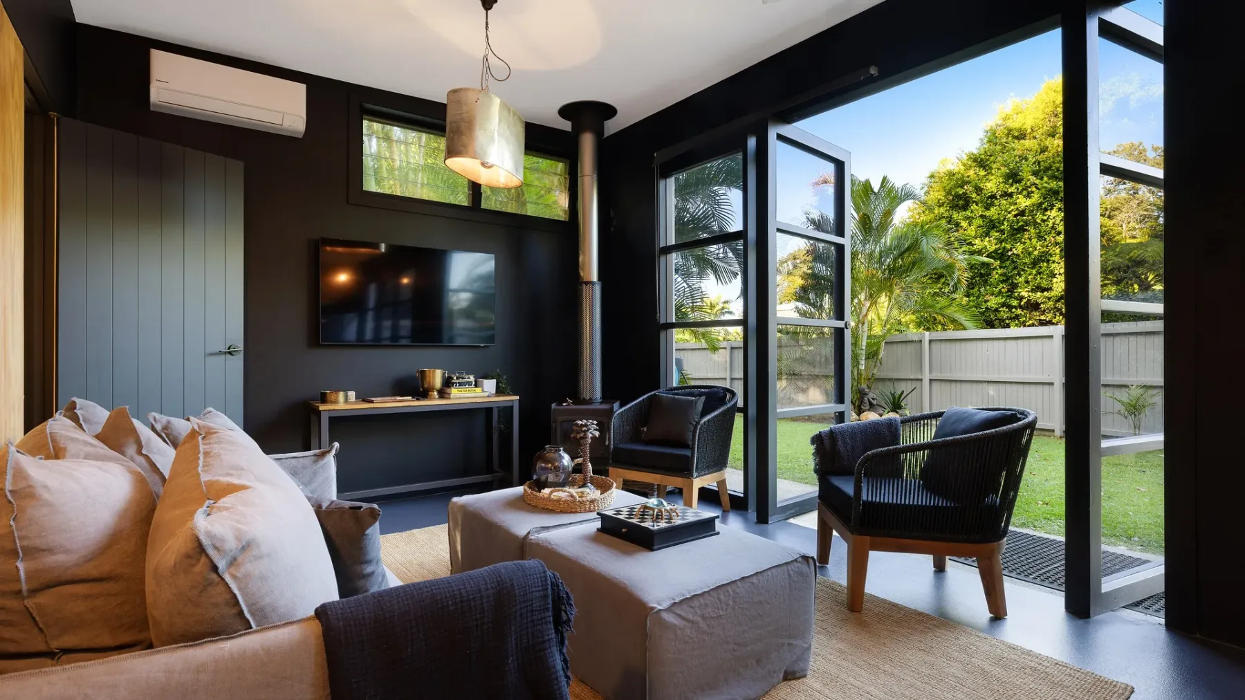 A modern living room with seating beside large glass doors opening to a garden.