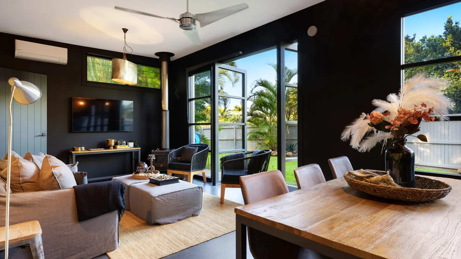 A living room with seating, a television, and large windows overlooking greenery.