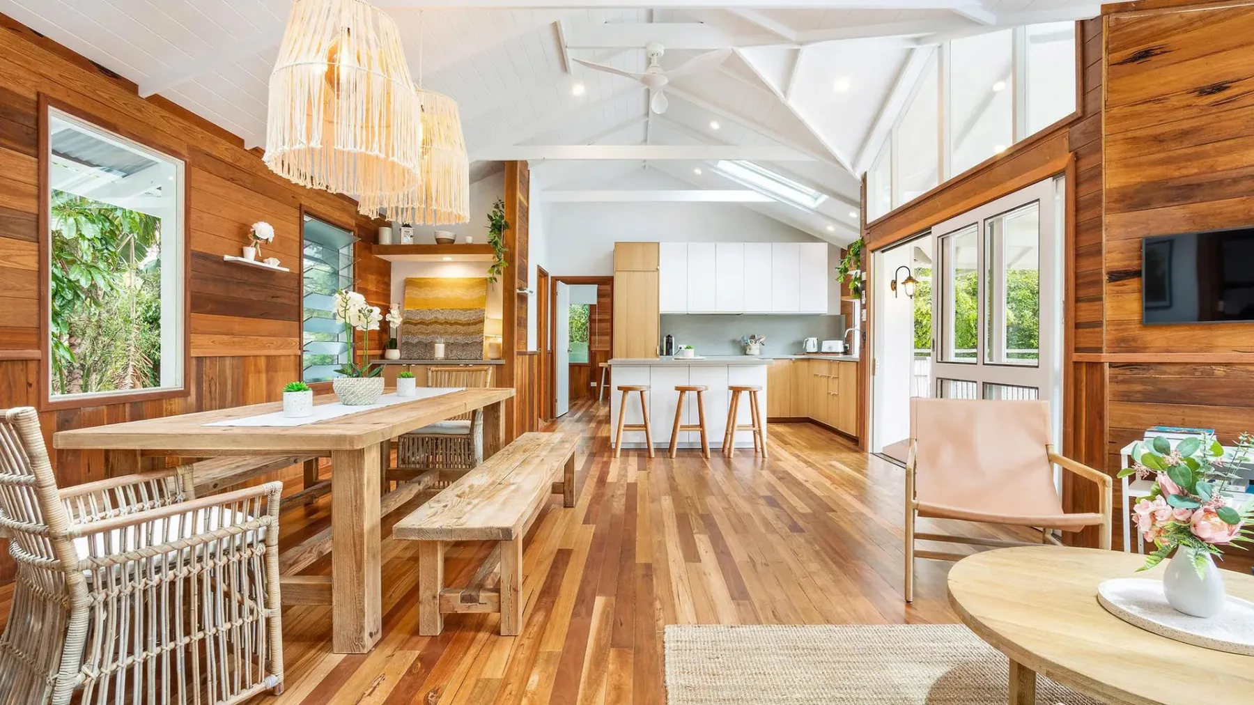 Un comedor y cocina de planta abierta, luminosos, con paredes de madera y una mesa larga.