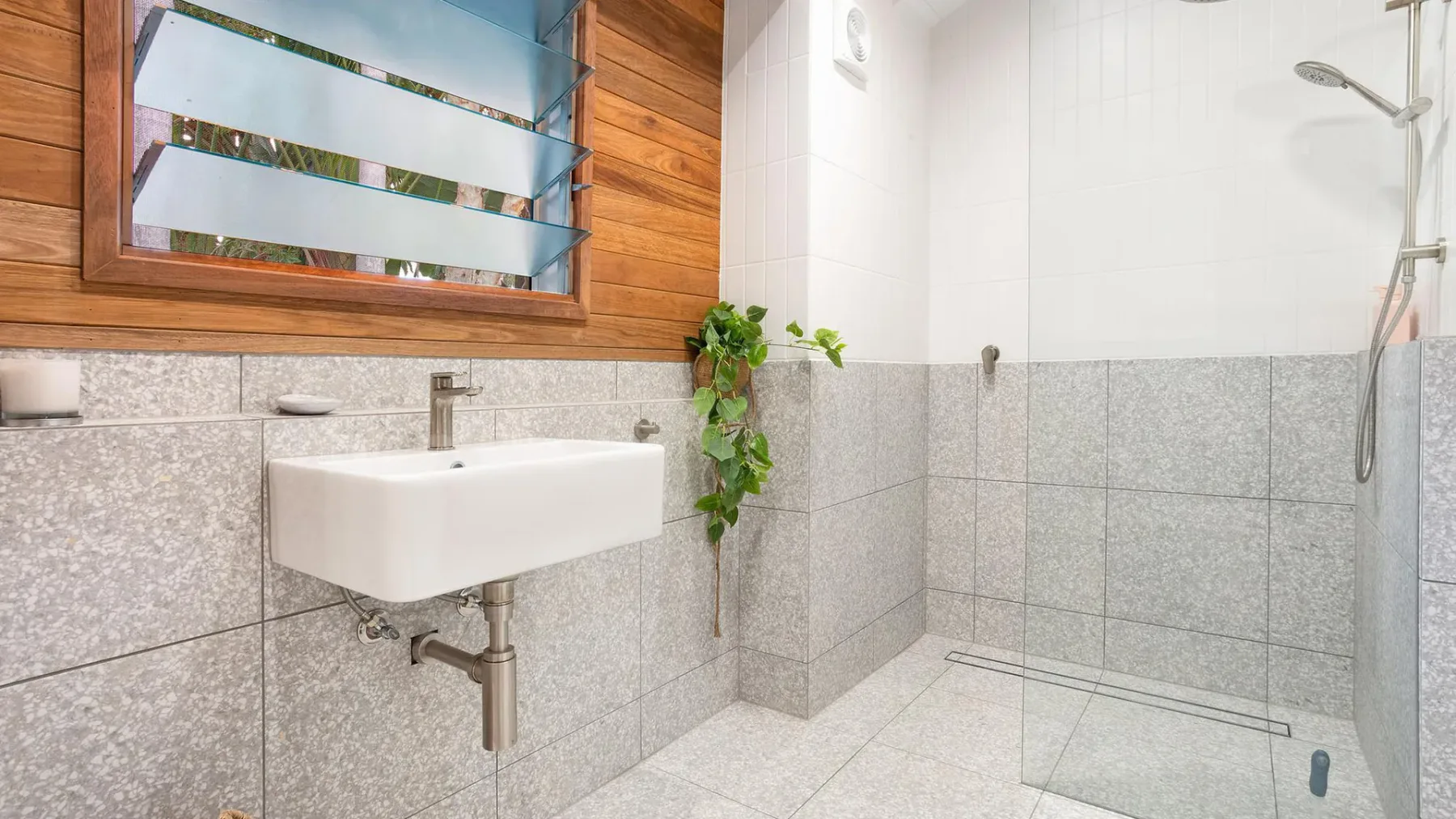 Un baño alicatado con lavabo de pared y ducha de vidrio.