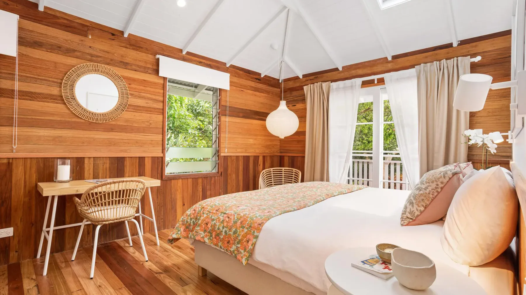 Un dormitorio luminoso con paredes de madera, una cama y un pequeño escritorio junto a la ventana.