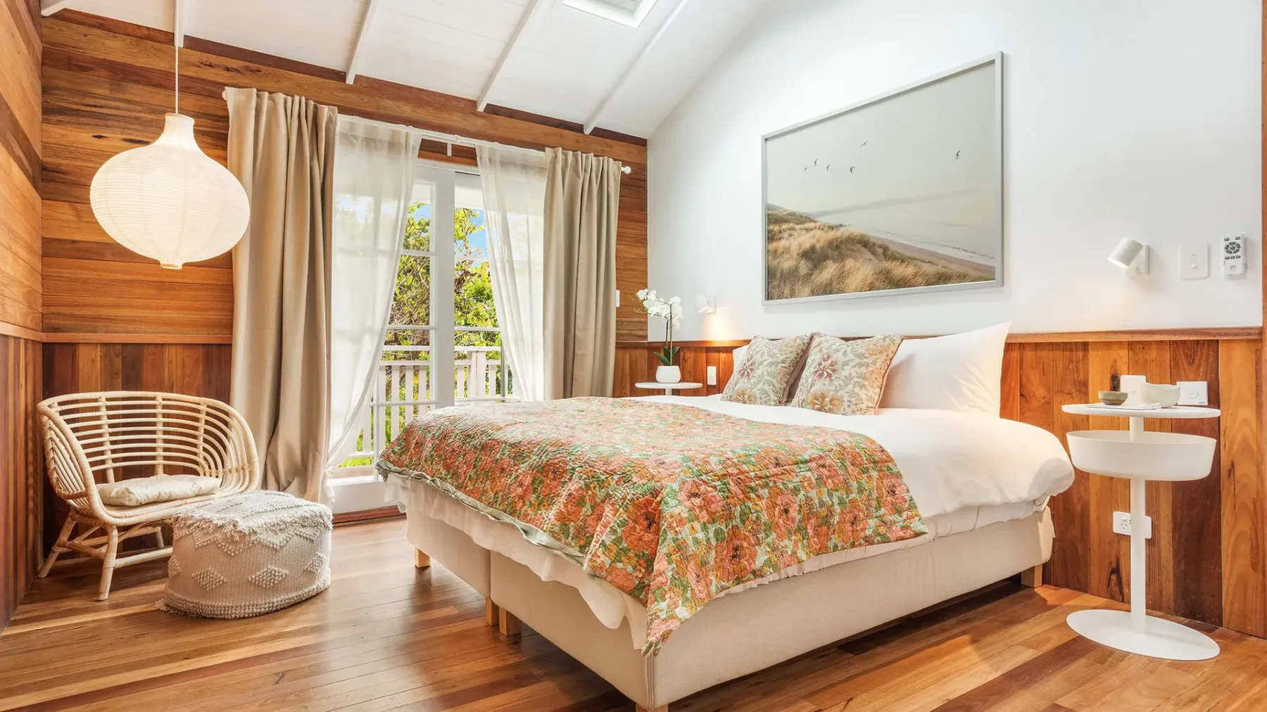 Un dormitorio luminoso con una cama cubierta por una colcha floral y una ventana al lado.