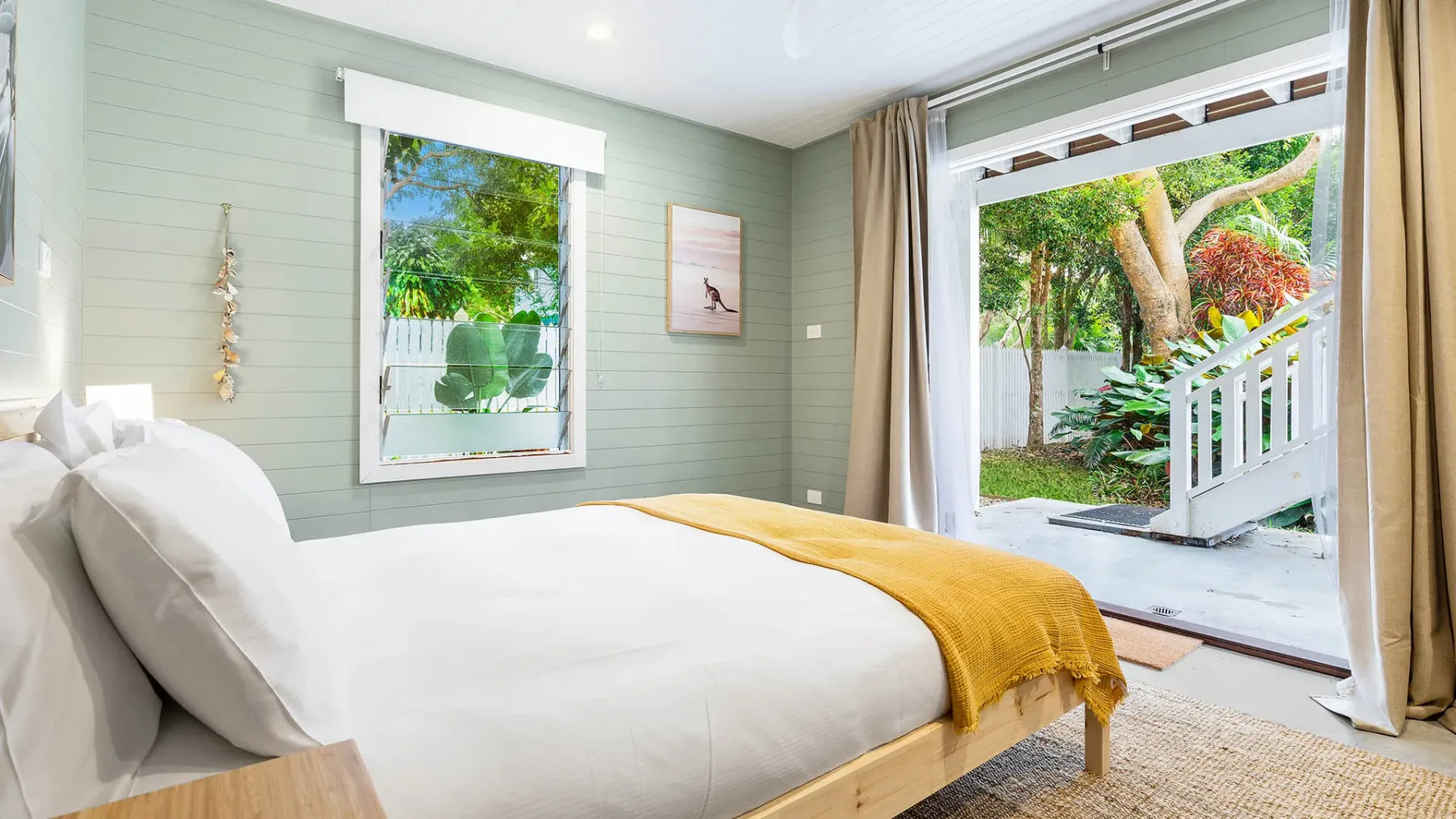 Un dormitorio luminoso con una cama junto a una puerta abierta al jardín.