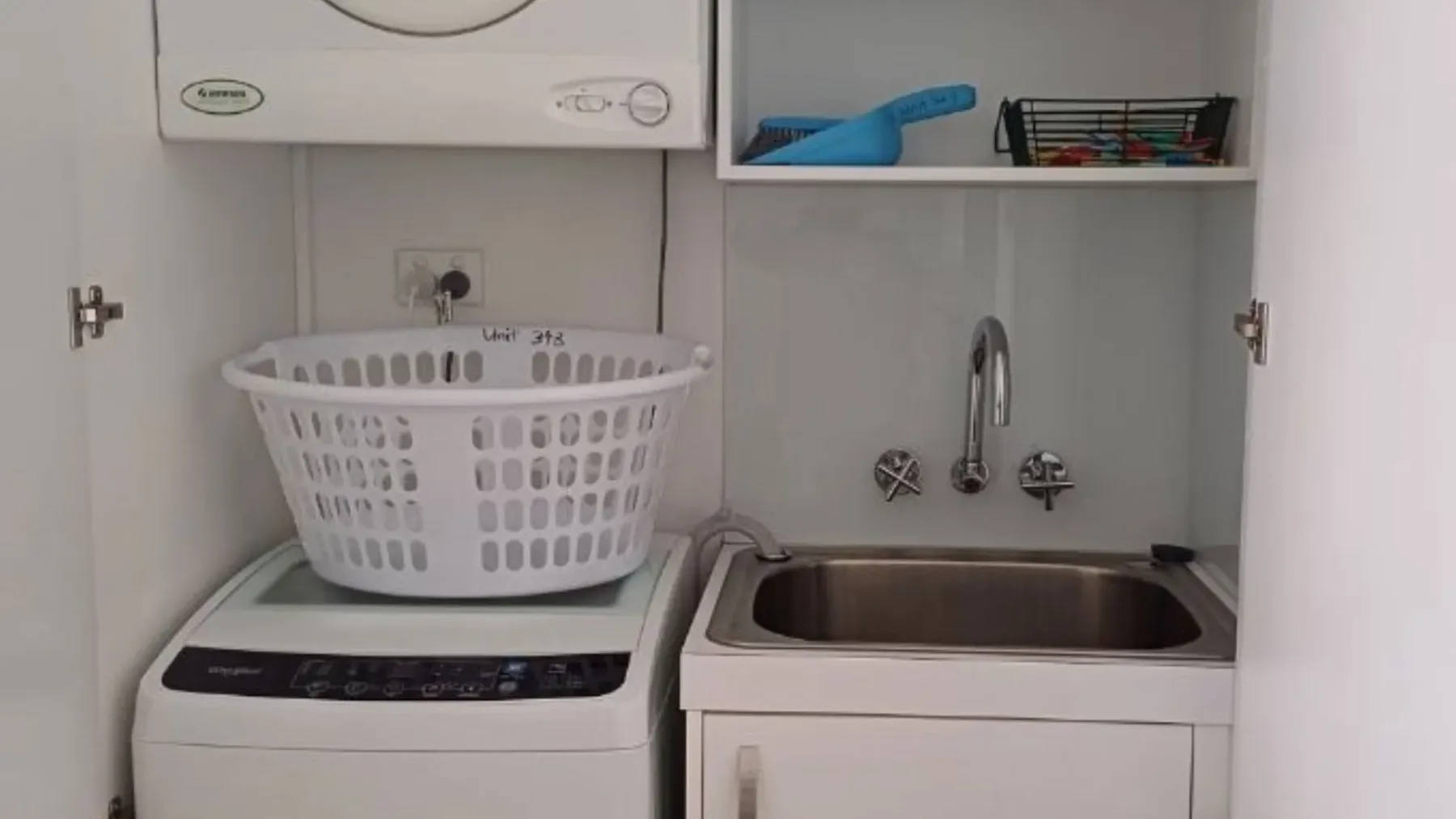 Un área de lavandería con lavadora, cesta de ropa y fregadero.