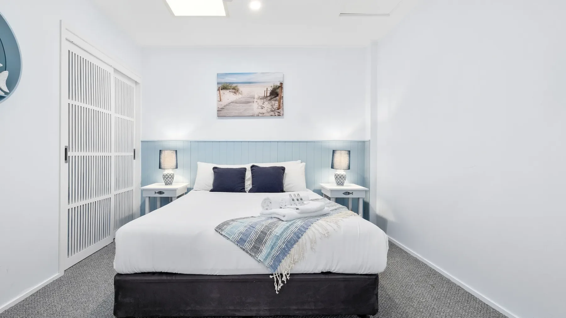 Un dormitorio luminoso con una cama bien tendida y una imagen enmarcada de la playa.