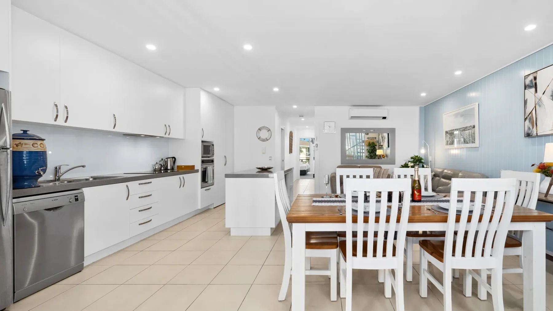 Una luminosa cocina abierta al comedor, con una mesa larga y asientos blancos.
