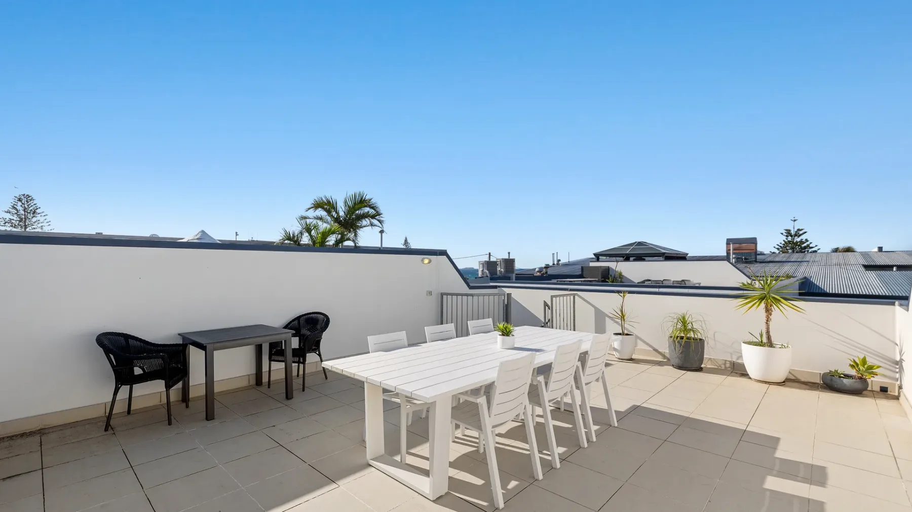 Una terraza en la azotea tiene mesas y sillas blancas junto a una pequeña zona de asientos.