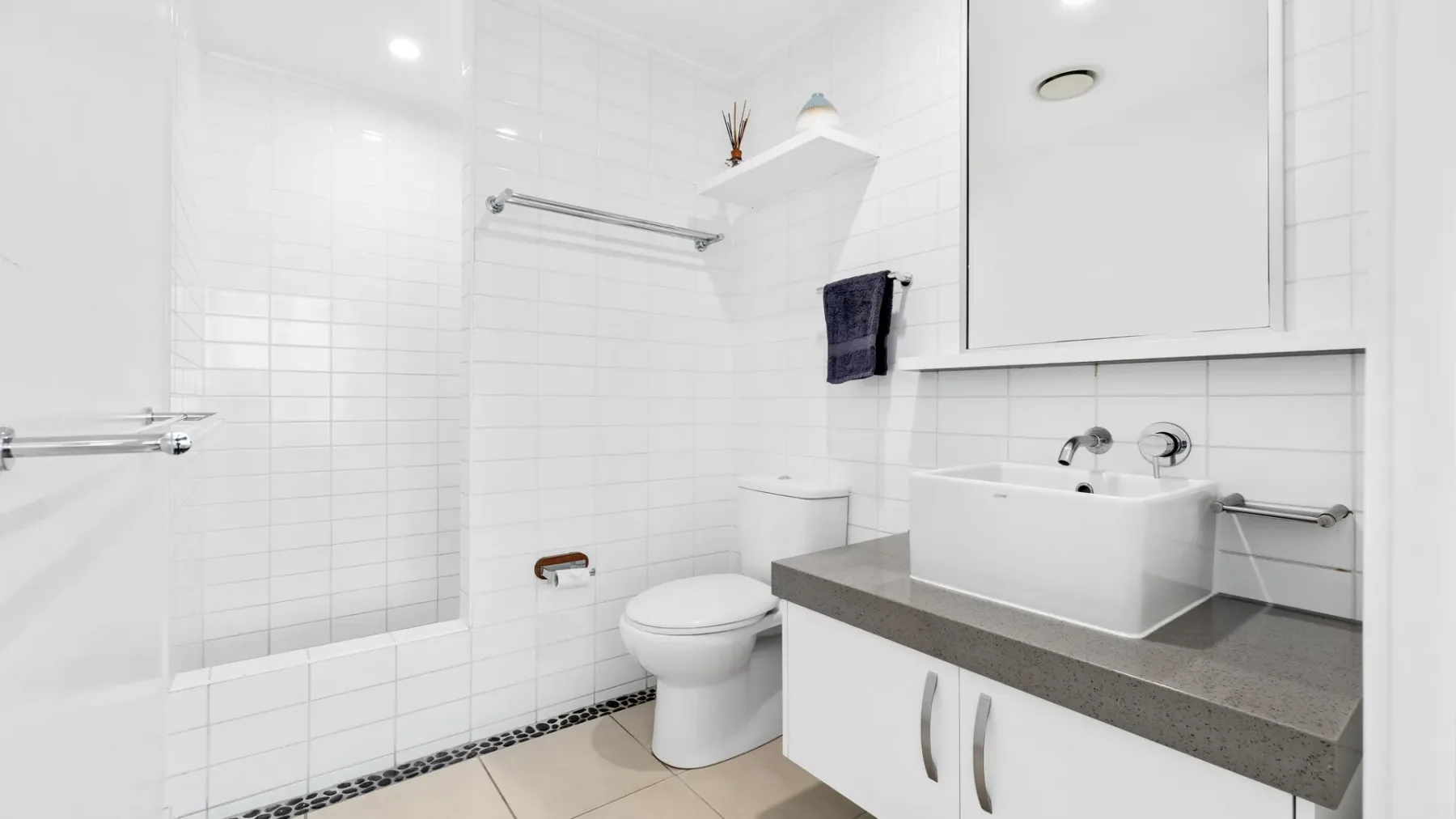 Un baño luminoso con azulejos, ducha, inodoro y lavabo.