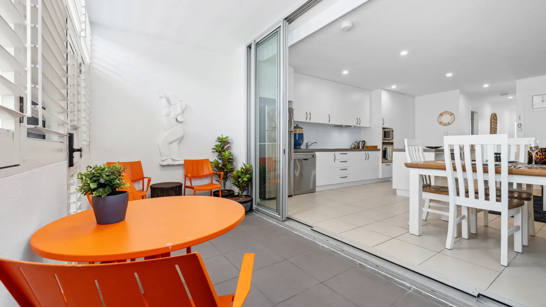 Una mesa naranja para comer al aire libre está junto a una cocina y comedor abiertos.