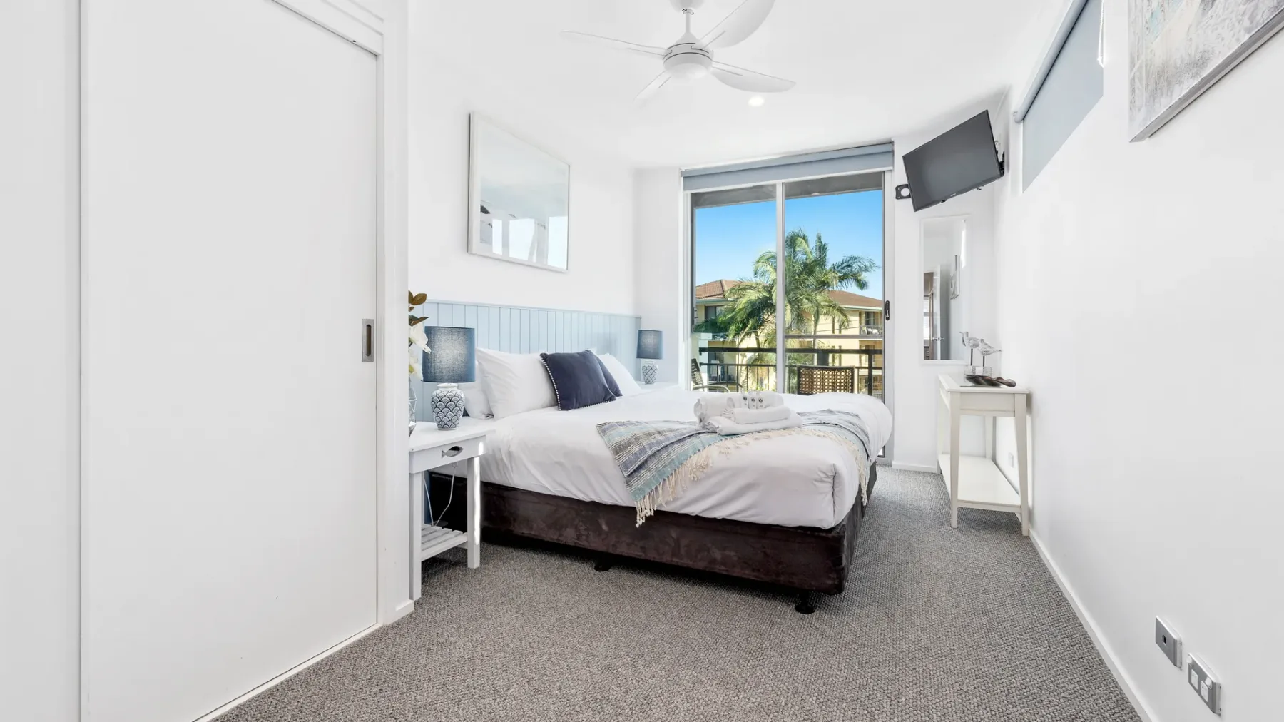 Un dormitorio luminoso con cama, asientos y una ventana con vista a palmeras.