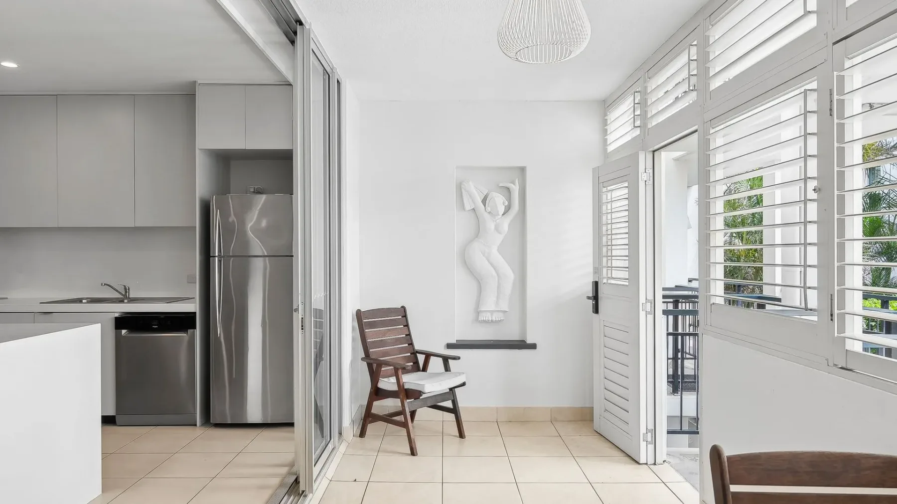Una cocina y comedor luminosos con una silla de madera junto a las puertas abiertas al patio.