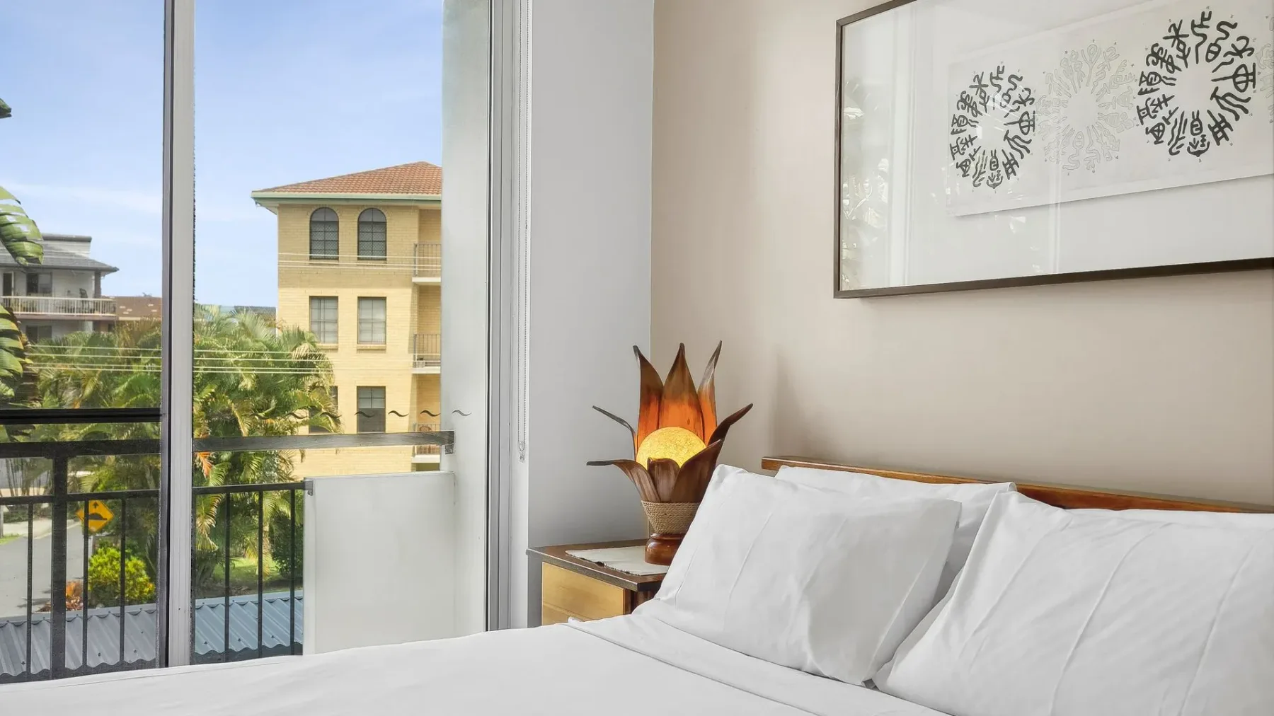A bedroom with a neatly made bed beside an open balcony door.