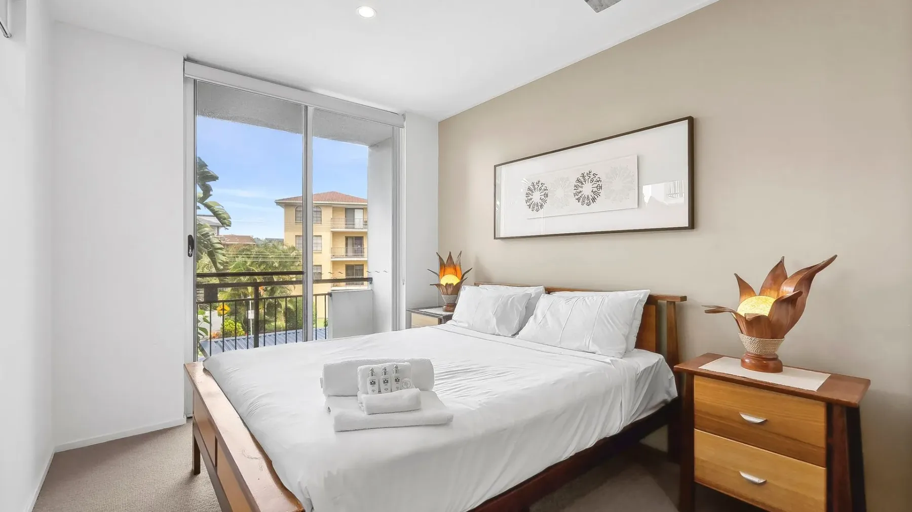A bright bedroom with a neatly made bed and framed artwork above it.
