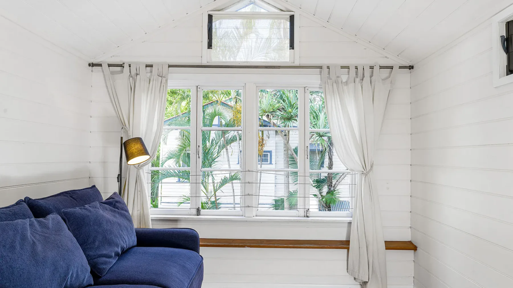 Una luminosa zona de estar con asientos azules junto a grandes ventanas con vistas a la vegetación.
