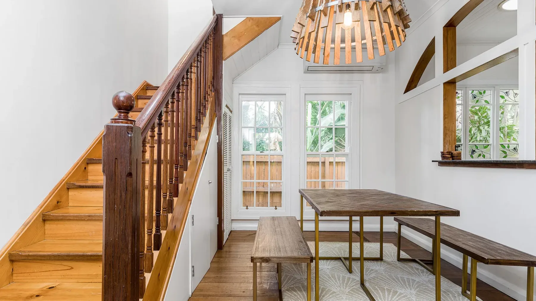 Un comedor luminoso con una mesa de madera y bancos junto a una escalera.