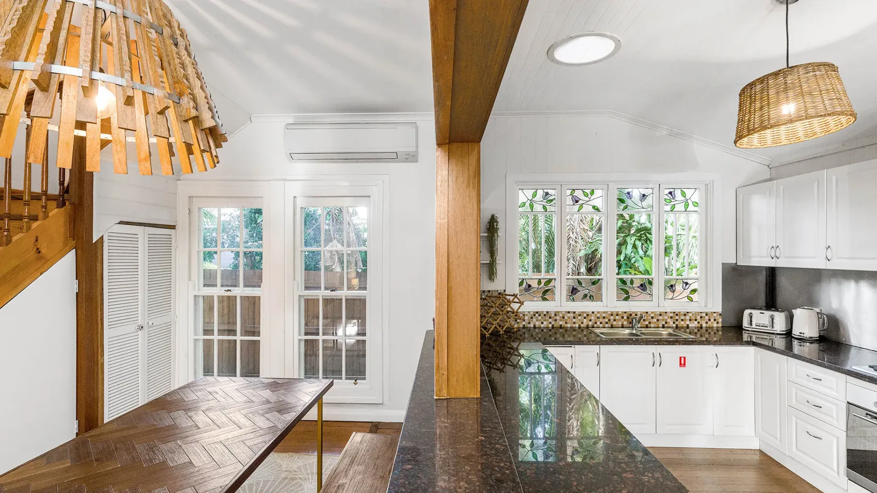 Una cocina luminosa con gabinetes blancos, una encimera oscura y una mesa de madera.
