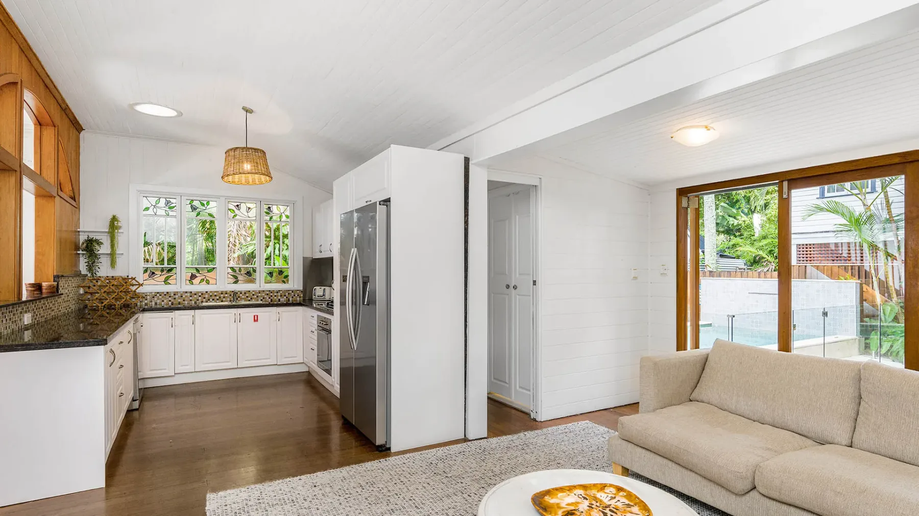 Una cocina luminosa y una zona de estar con gabinetes blancos y un sofá beige.