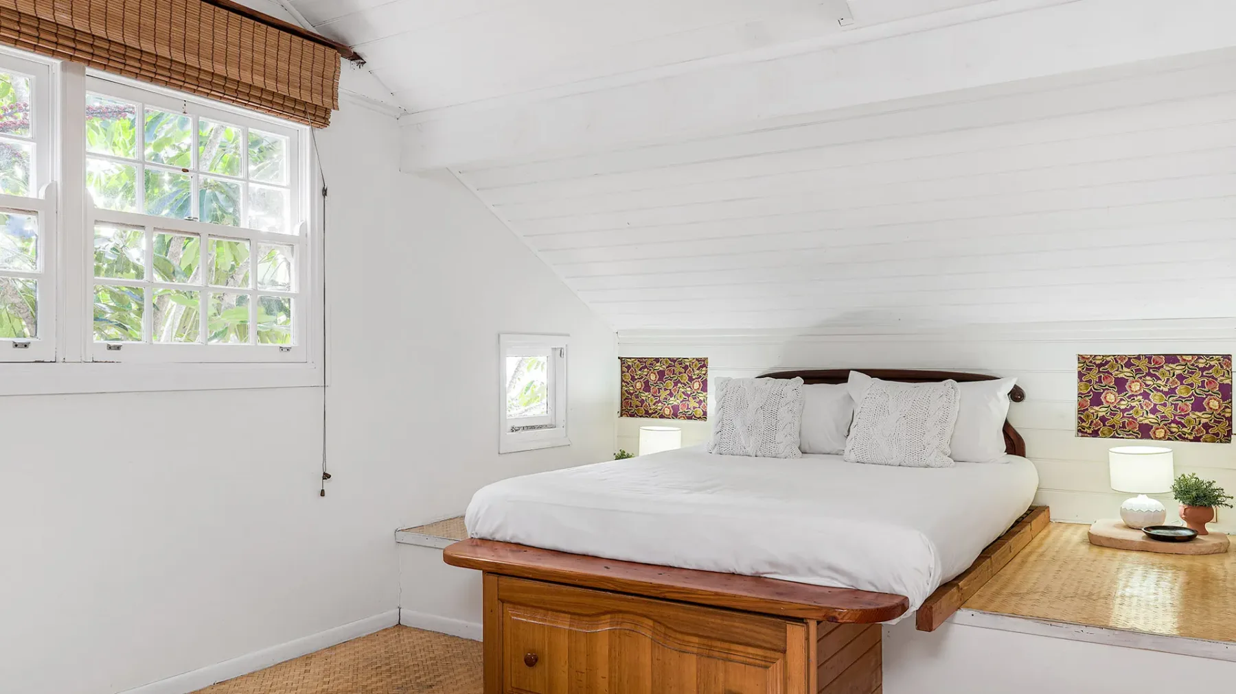 Un dormitorio luminoso con una cama bien tendida bajo un techo inclinado.