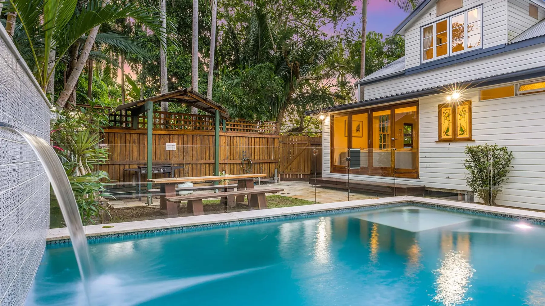 Una piscina exterior junto a una casa blanca y un refugio de jardín de madera.