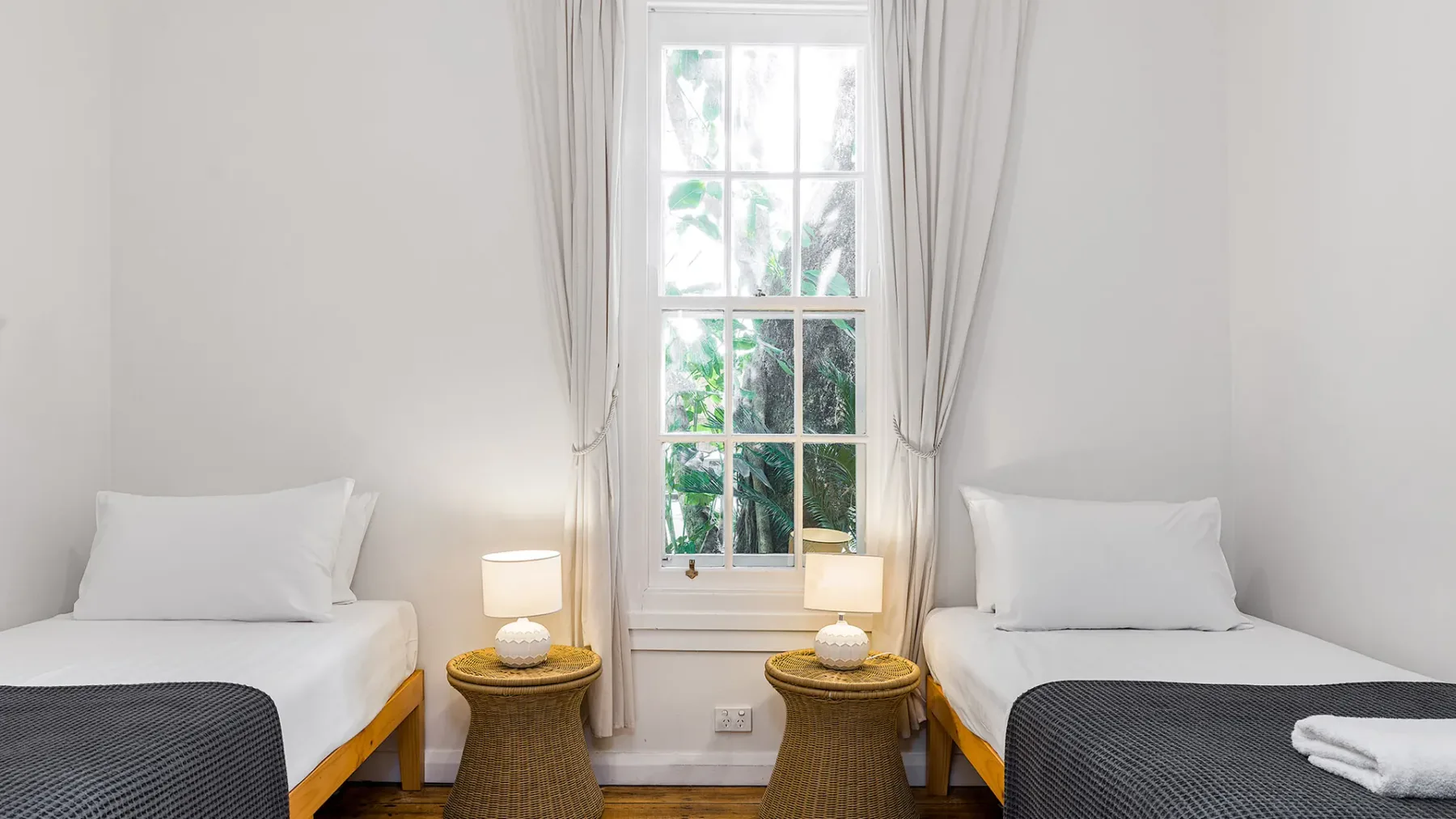 Un dormitorio luminoso con dos camas individuales junto a una ventana alta.