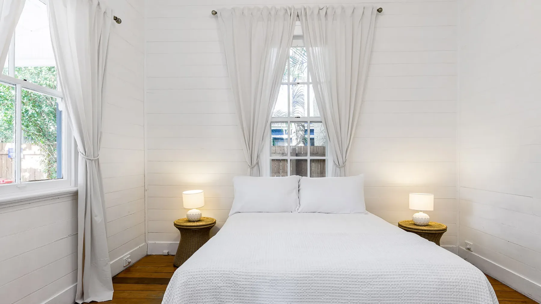 Un dormitorio con una cama centrada bajo una ventana con cortinas.