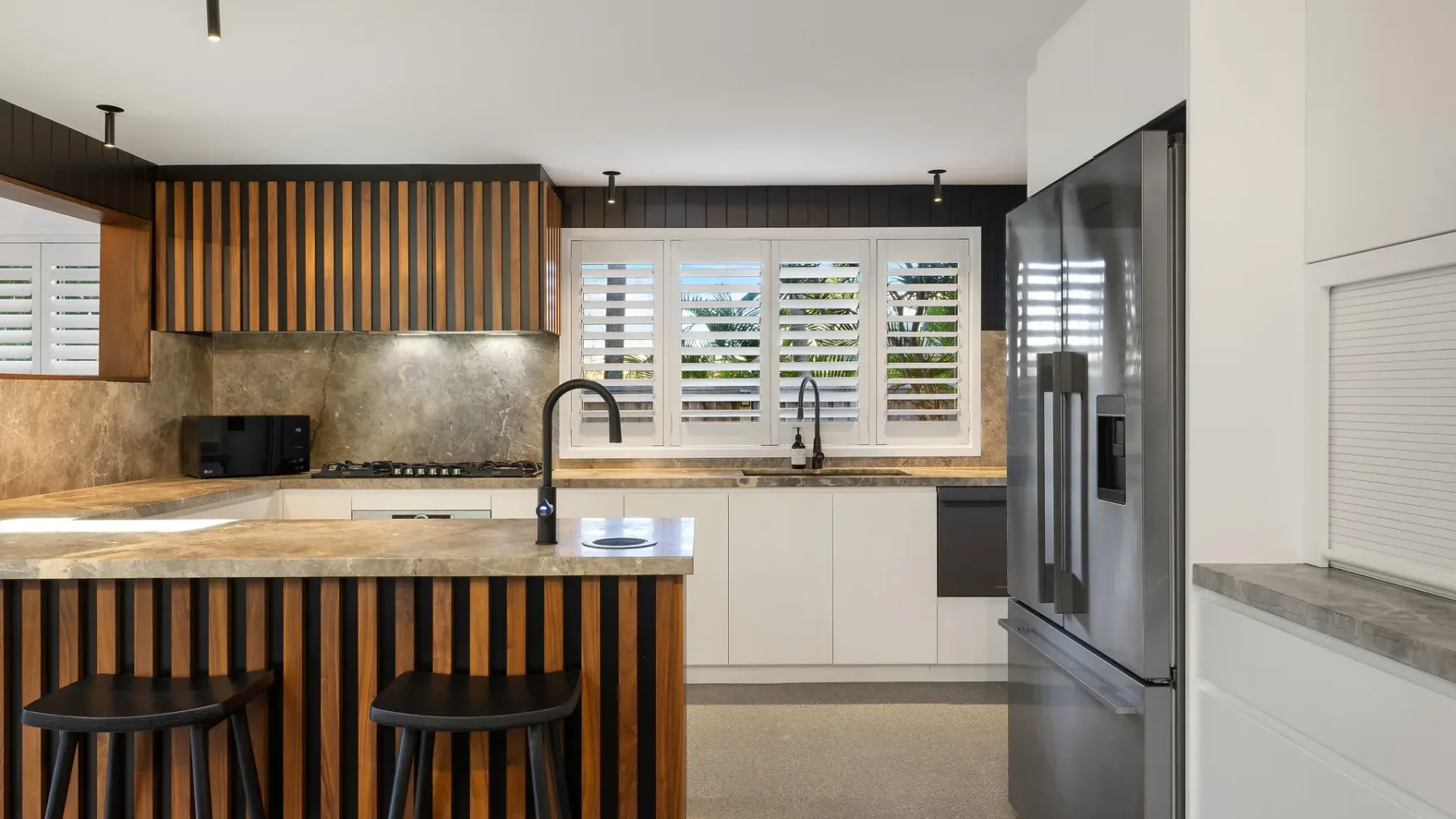 Una cocina moderna con isla central, gabinetes oscuros y ventanas amplias.