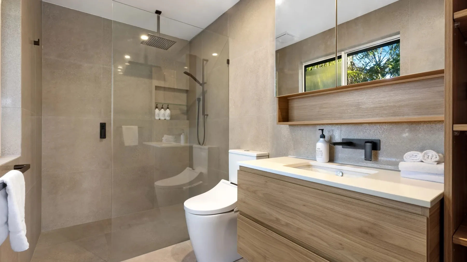 Un baño moderno con ducha de vidrio y un mueble de madera bajo un espejo amplio.