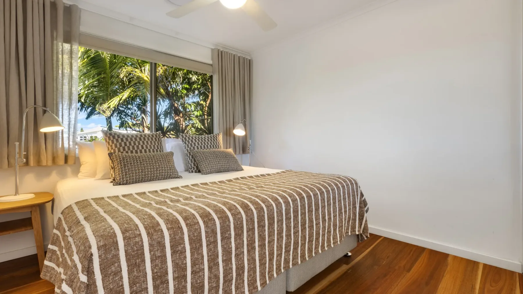 Un dormitorio con una cama junto a una ventana grande con árboles frondosos a la vista.