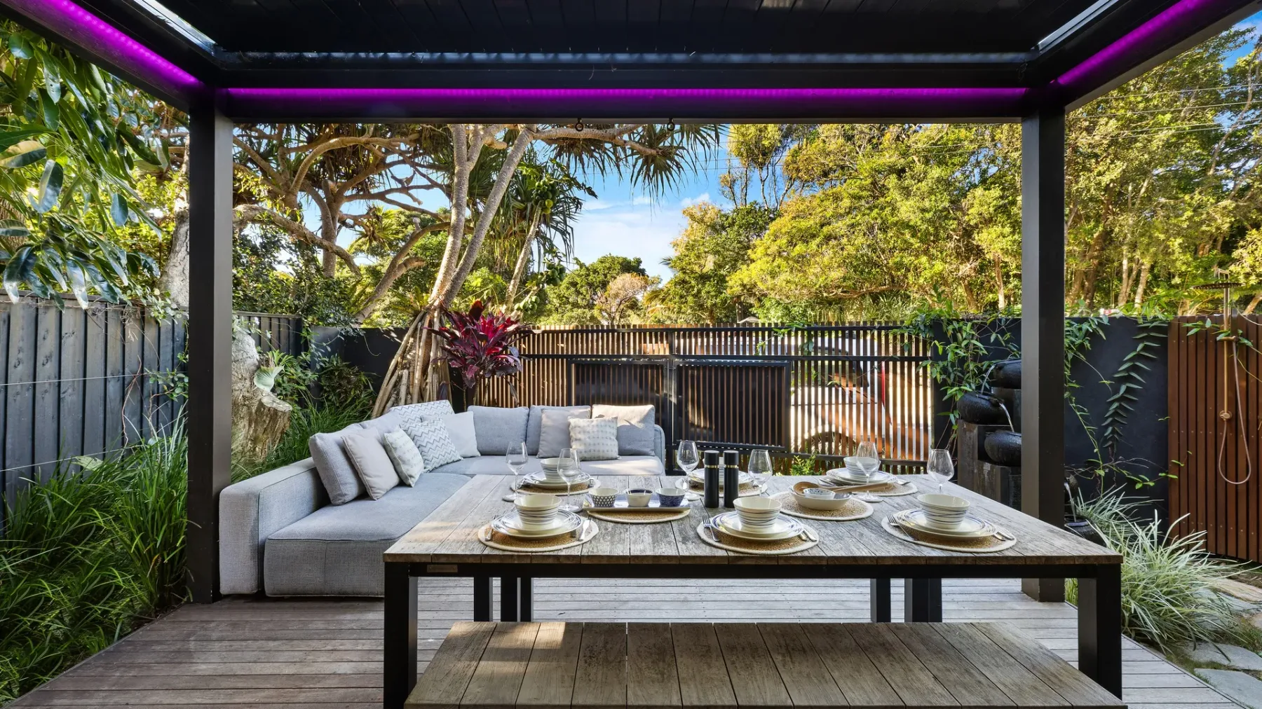 Comedor exterior cubierto con una mesa larga y asientos acolchados.