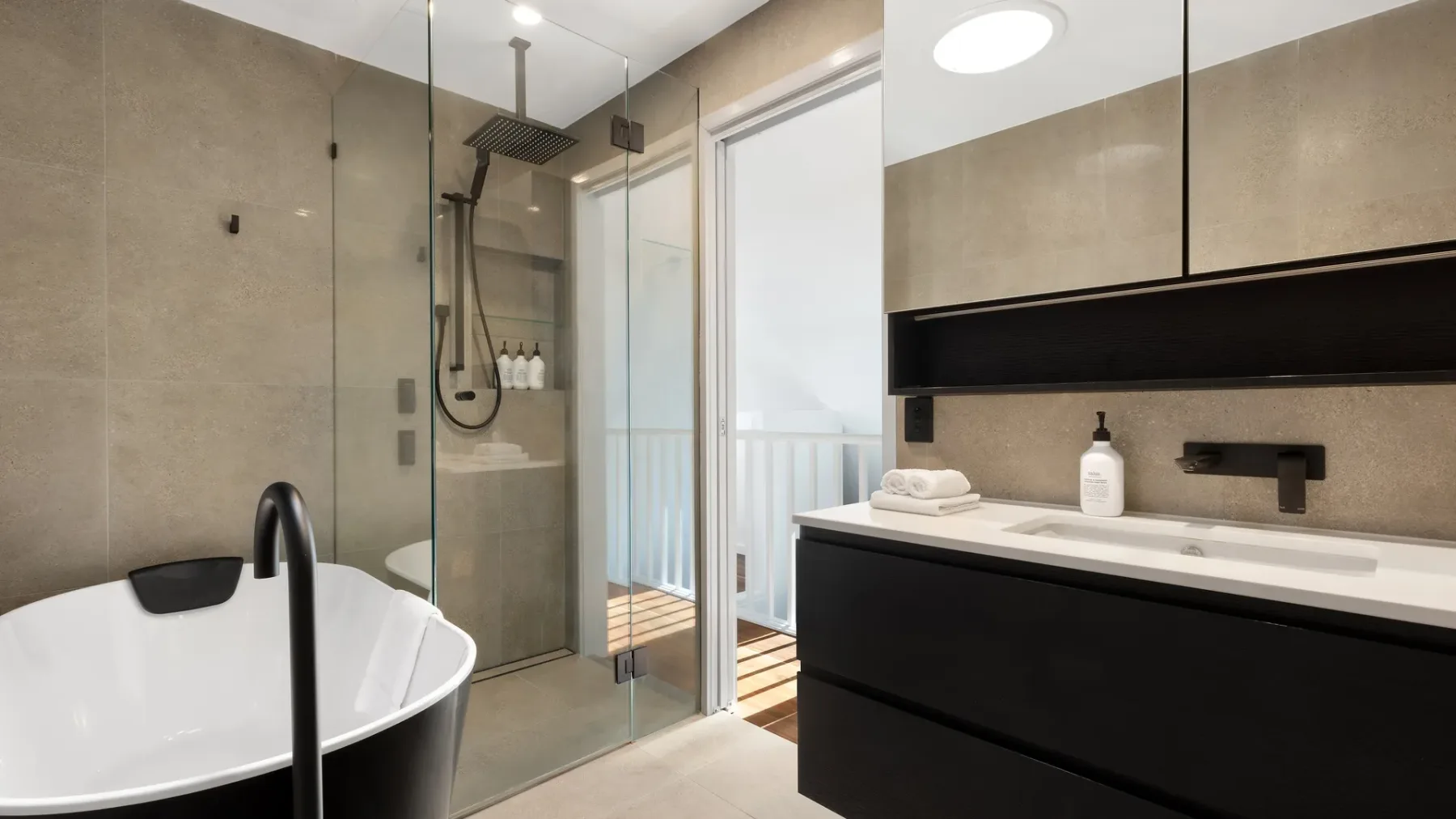 Un baño moderno con bañera, ducha de vidrio y tocador oscuro.