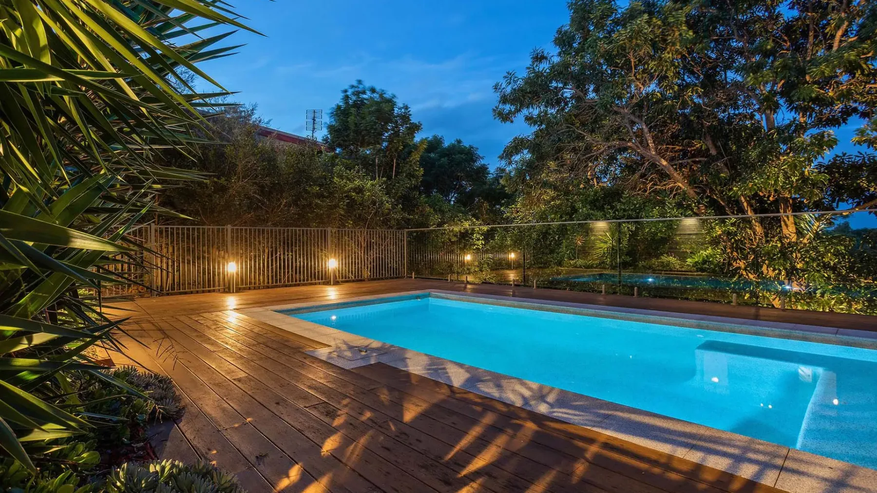 A swimming pool sits beside a wooden deck, surrounded by trees.