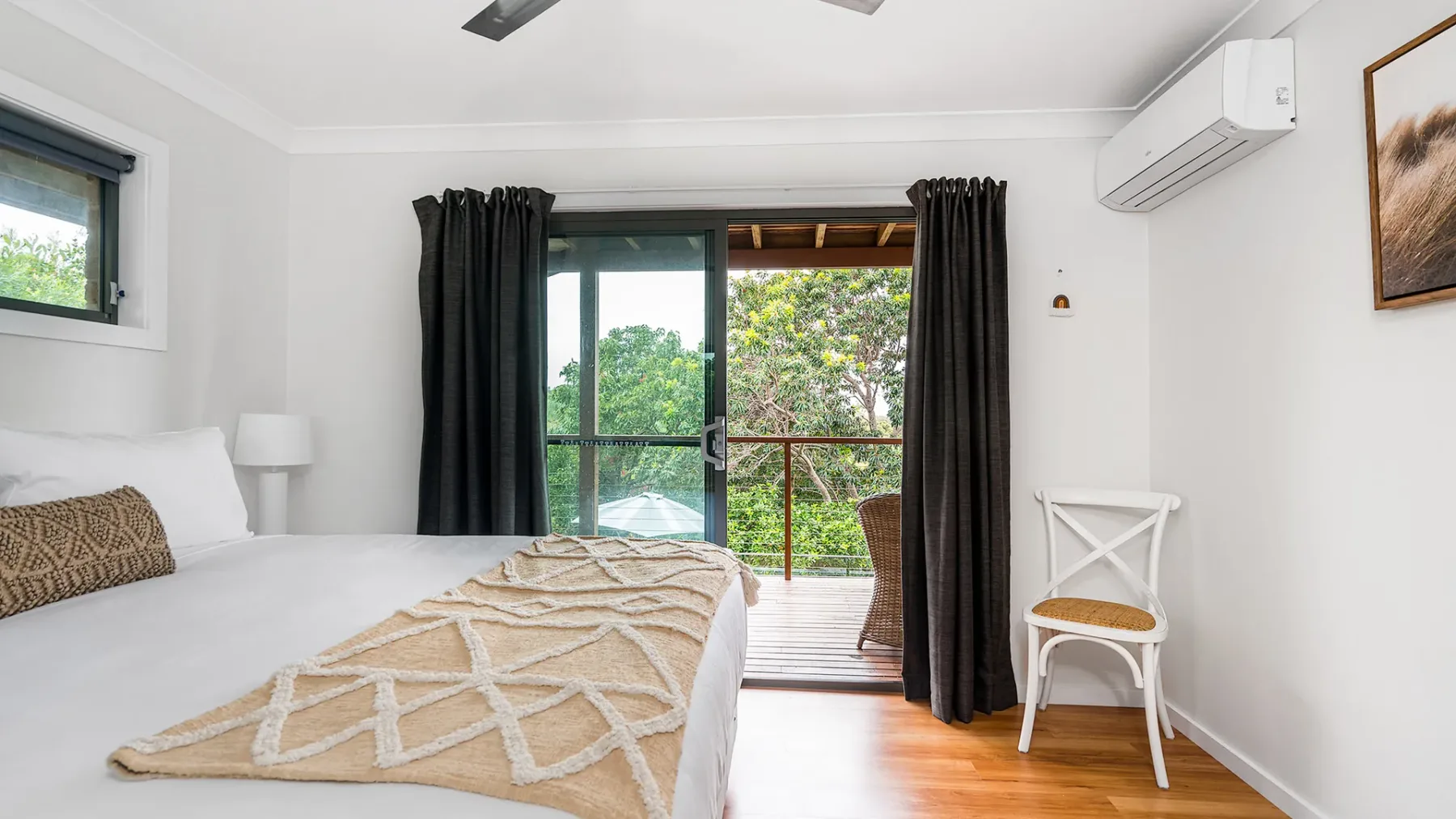 A bright bedroom with a bed beside sliding glass doors opening onto a balcony.