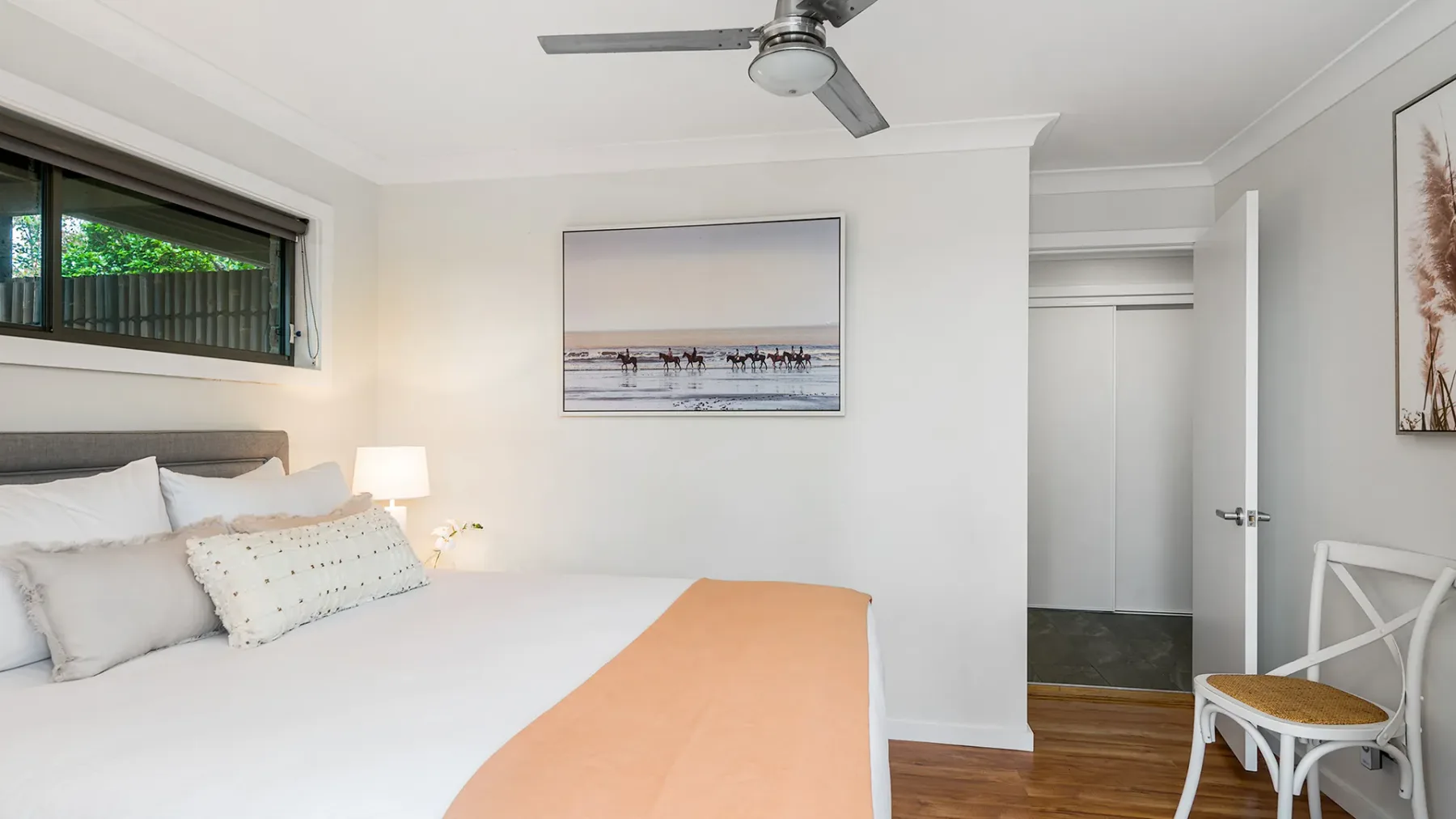 A bright bedroom with a neatly made bed and framed artwork.