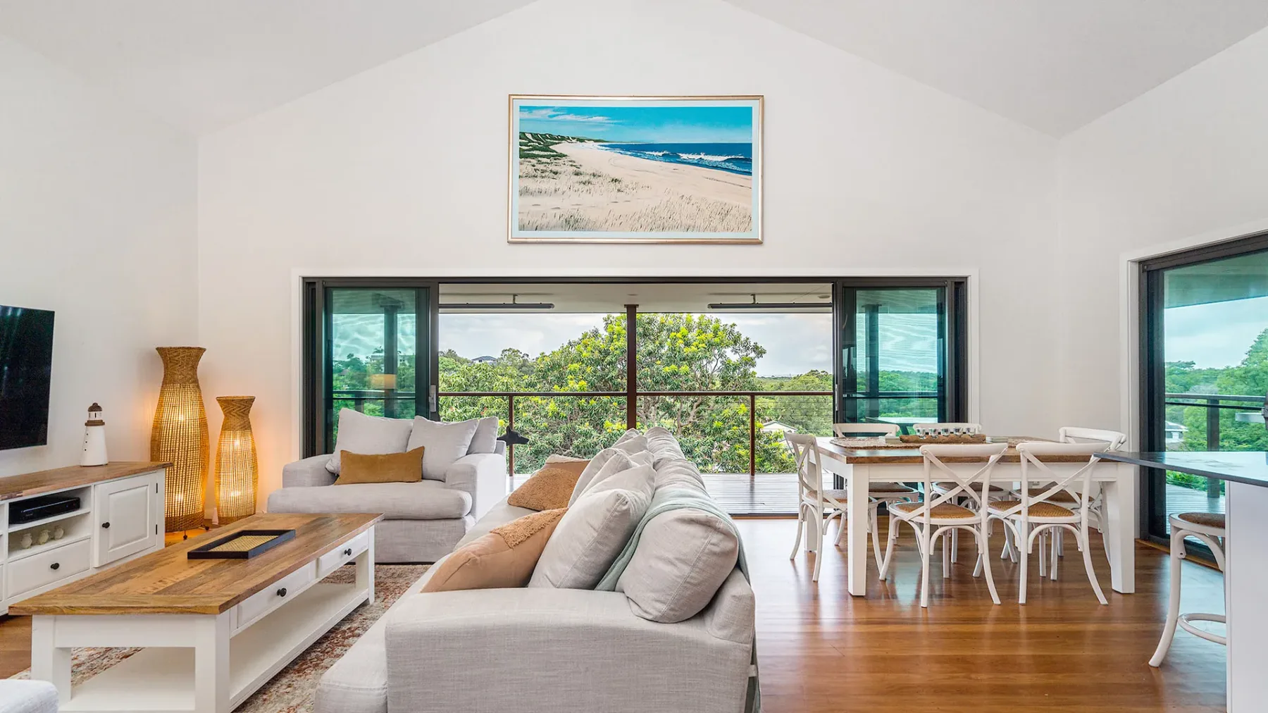 A bright living and dining area opens onto a balcony, with greenery visible outside.