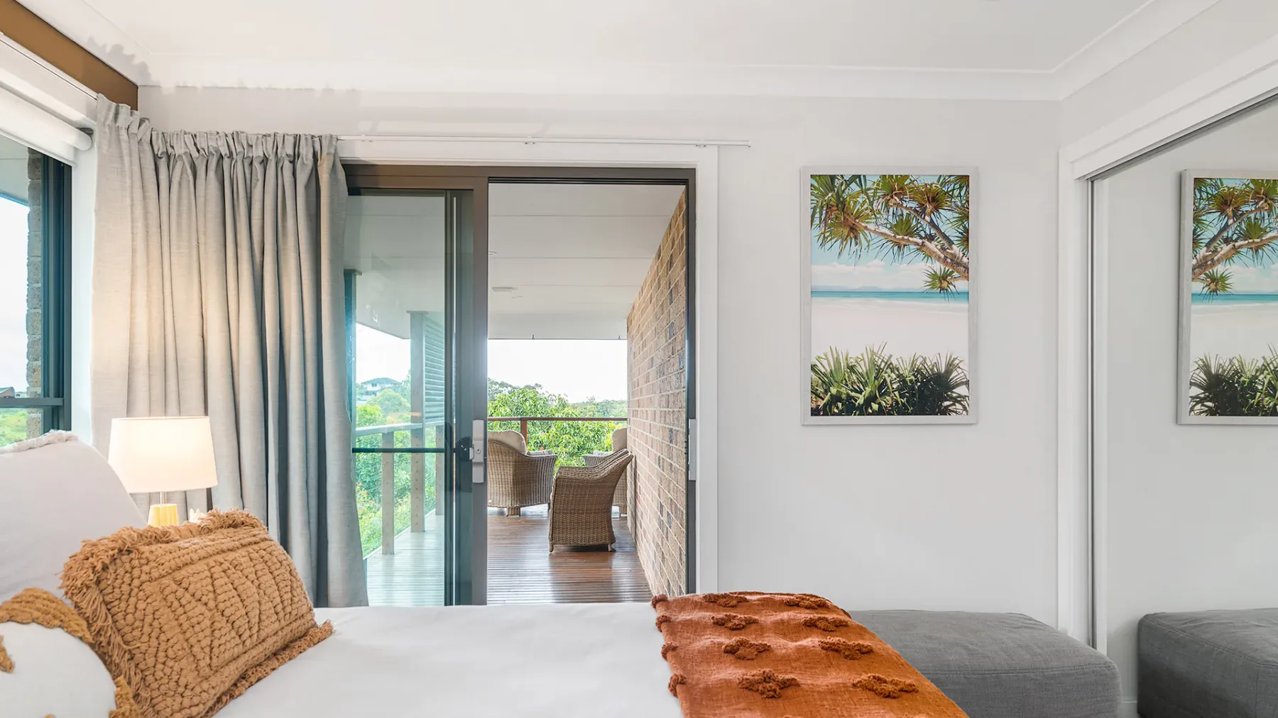 A bright bedroom opens onto a balcony through sliding glass doors.