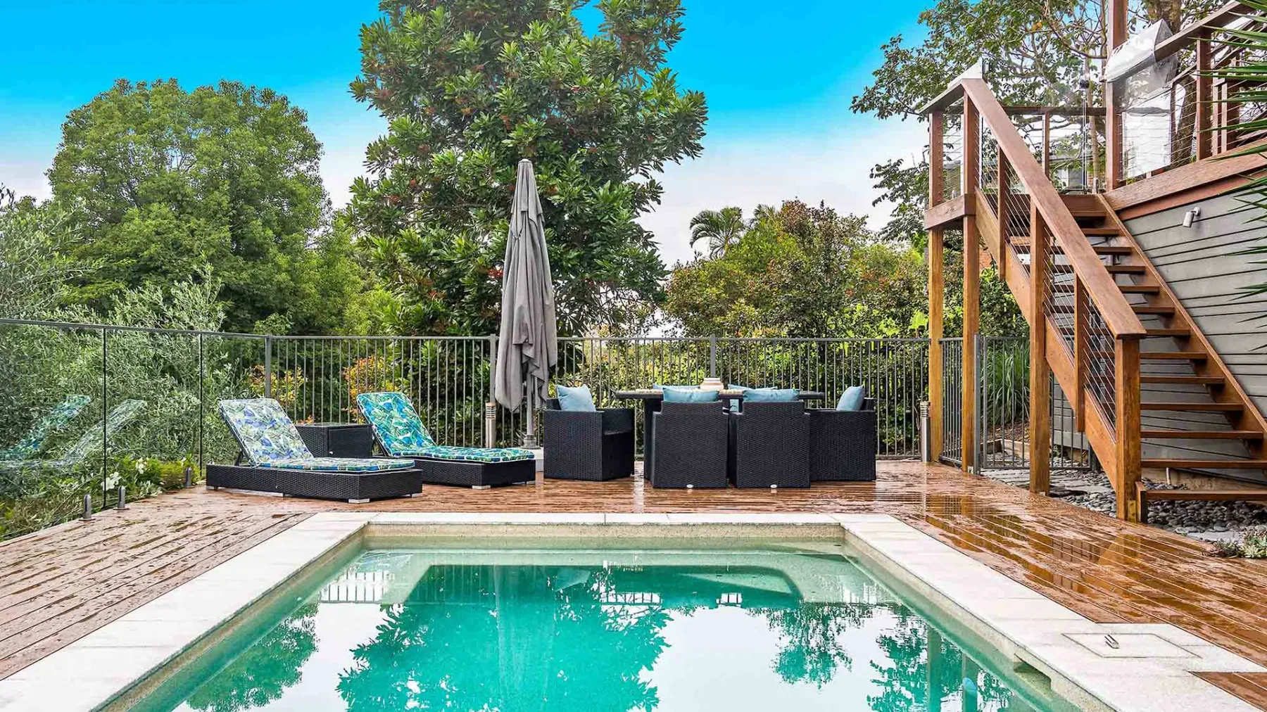An outdoor pool beside a wooden deck with seating and stairs.