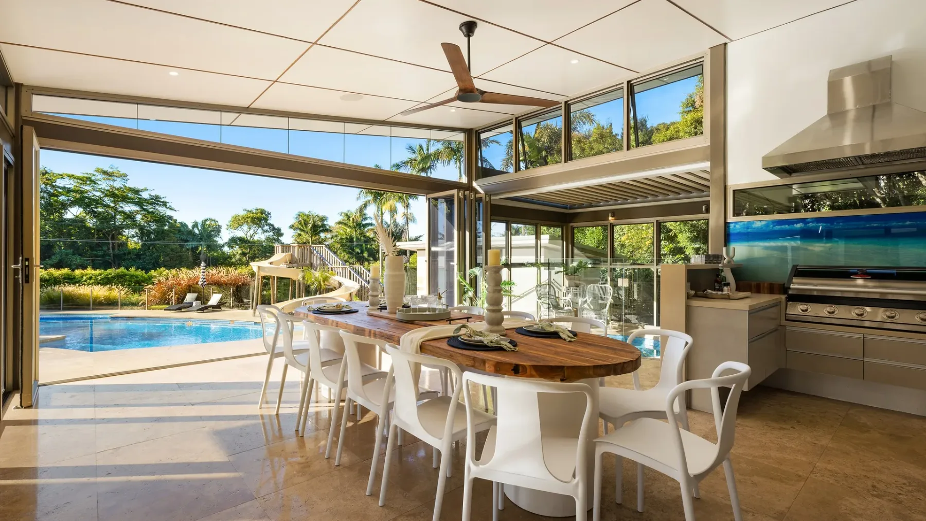 Un comedor luminoso se abre a una piscina y un jardín frondoso.
