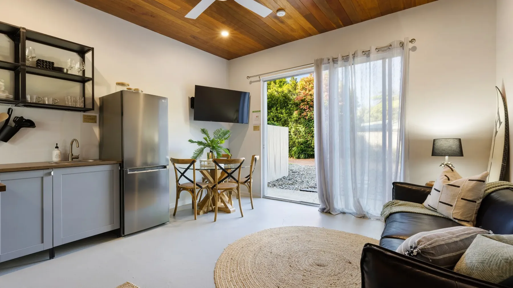 Una luminosa sala de estar con mesa de comedor, cocina pequeña y puertas corredizas de vidrio.