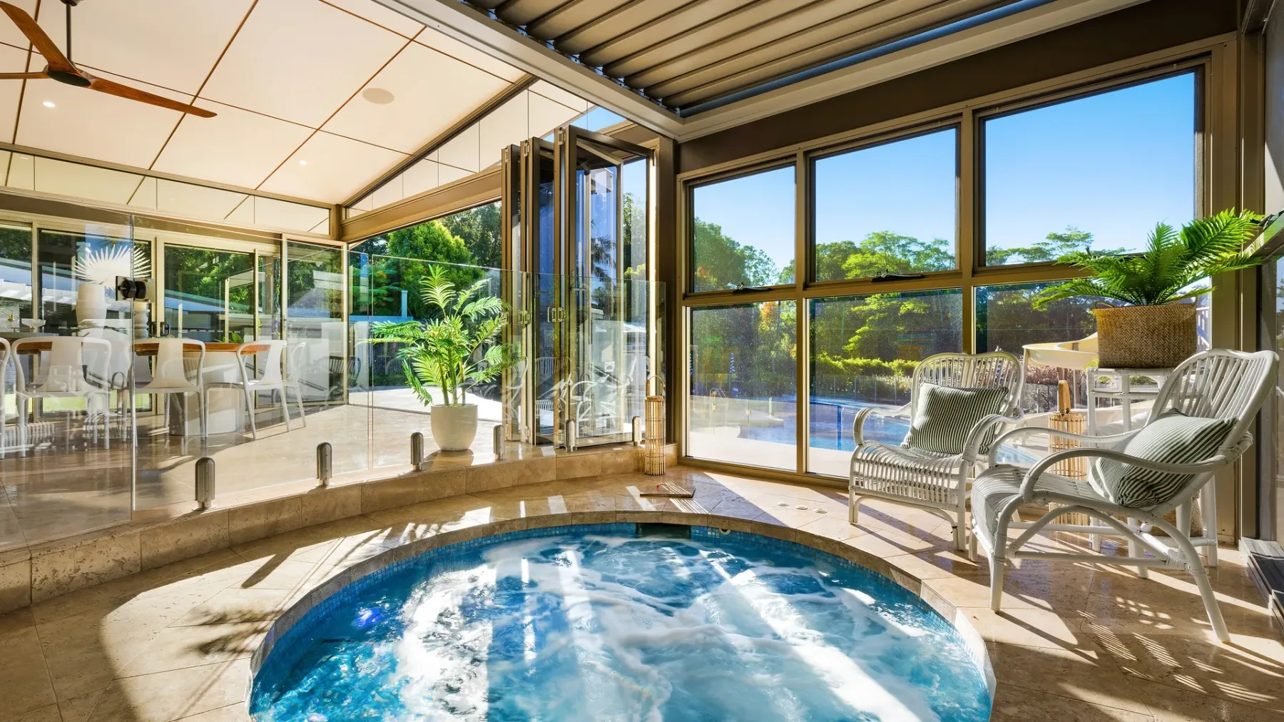 Una luminosa zona de piscina interior se abre a un comedor acristalado y un jardín.