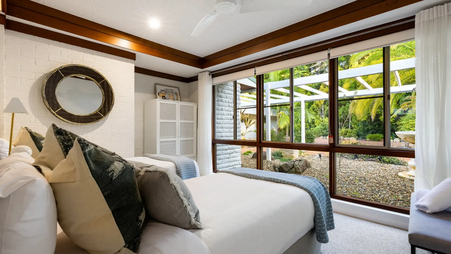 Un dormitorio con una cama bien tendida junto a grandes ventanas con vistas a un jardín.